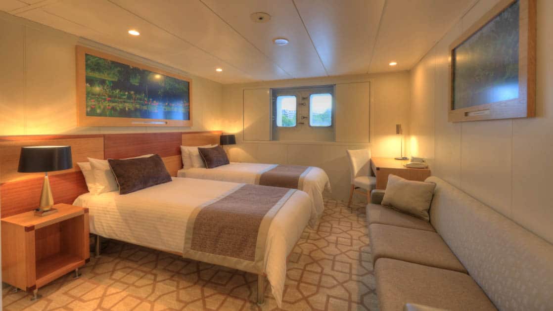 Main Deck stateroom aboard Coral Discoverer with two twin beds, couch, and window.