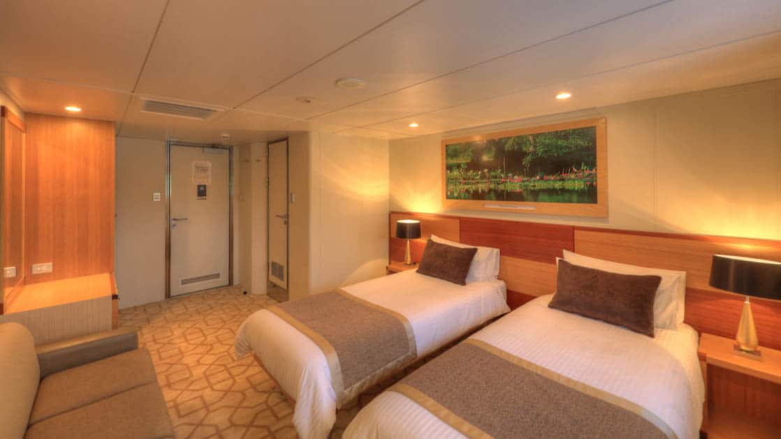 Main Deck stateroom aboard Coral Discoverer with two twin beds, couch, and doorway..