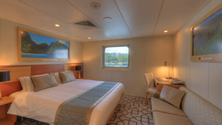 Promenade Deck stateroom aboard Coral Discoverer with bed, couch, and window.