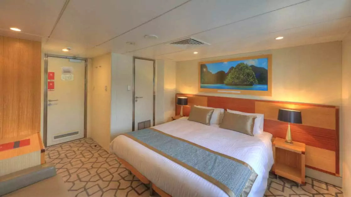 Promenade Deck stateroom aboard Coral Discoverer with bed, couch, and doorway.