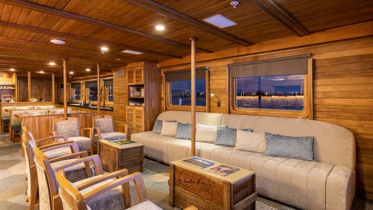 Interior lounge with couches, coffee tables, large windows, and chairs Interior of Junior Cabin with queen bed, bench and three large windows aboard Coral I & Coral II yachts in the Galapagos Islands