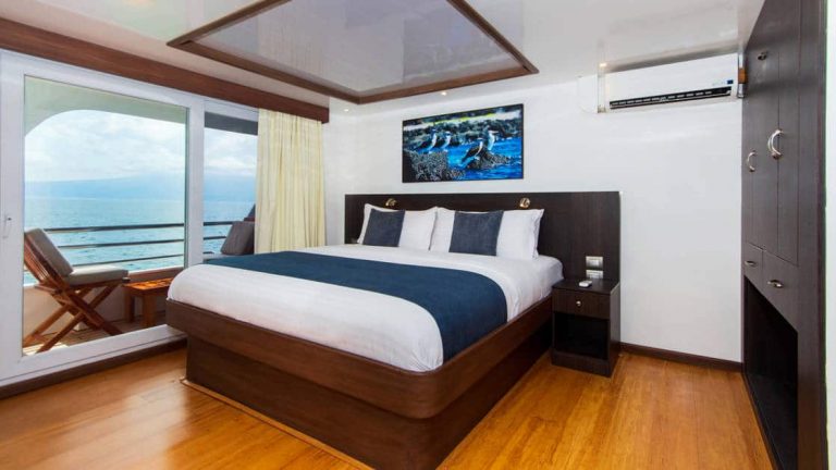 double bed with large windows and balcony with lounge chair outside aboard the Cormorant in the Galapagos