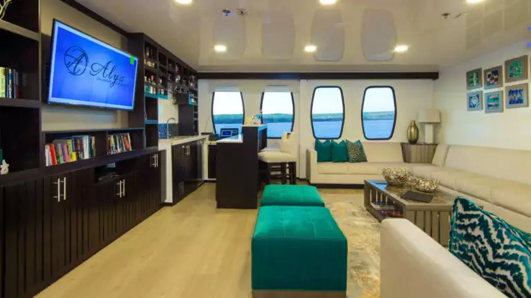 Lounge aboard Alya with couches, windows, and big screen tv.