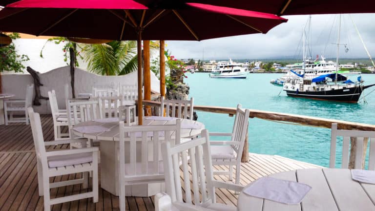 White tables and chairs on the outdoor patio overlooking bright blue teal waters of the harbor in the Galapagos