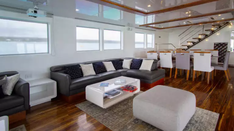 Galapagos Infinity lounge with comfortable couches, chairs, ottoman, large windows and coffee table.