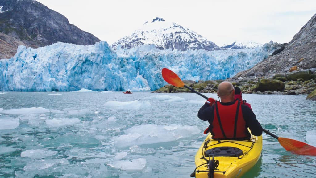 man kayaking in alaska with a glacier in front of him