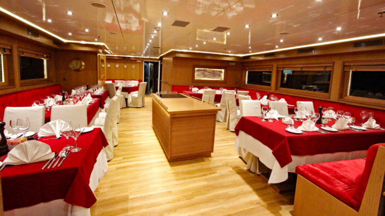 Harmony G yacht dining room with tables and chairs set up for a meal and windows.