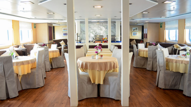 Harmony V yacht dining room with tables set up for a meal, chairs and large windows.