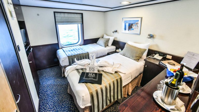 Harmony V Category P stateroom with 2 twin beds, nightstand, couch seating, dresser, large window and night lights.