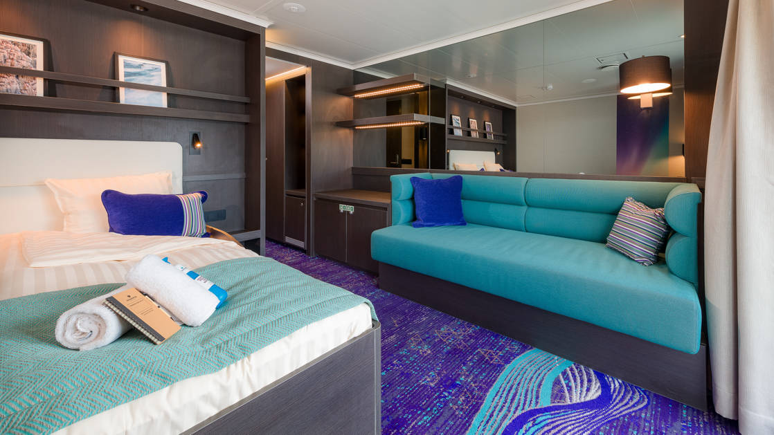 Grand Suite aboard Hondius and Janssonius polar small ships, with teal and purple accents, couch, double bed & bookshelves.