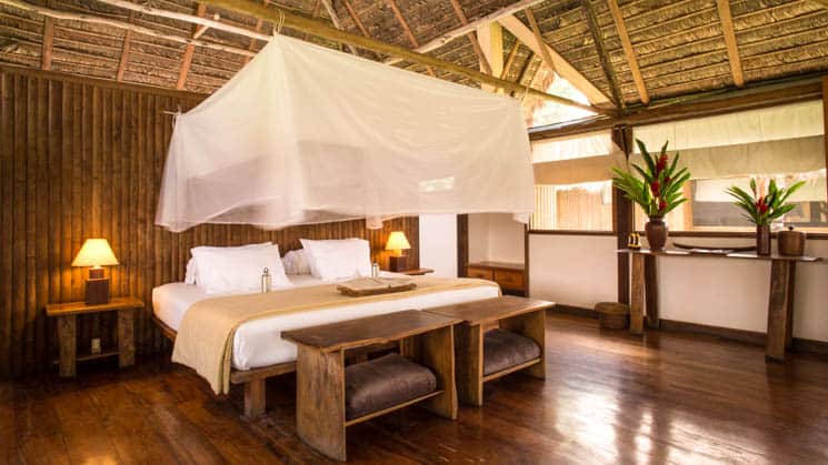 A king bed with a mosquito net, reading lights, open windows at the Tambopata Suite at Inkaterra Reserva Amazonica, an eco-luxury lodge in Peru.