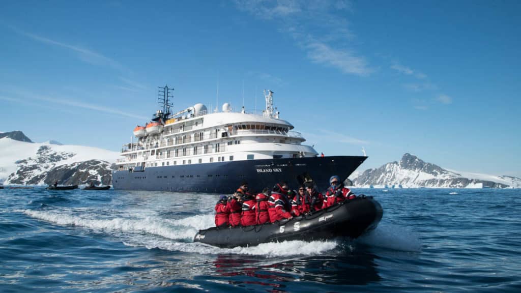 Island Sky anchored off the coast of Antarctica with a zodiac cruising with passengers.