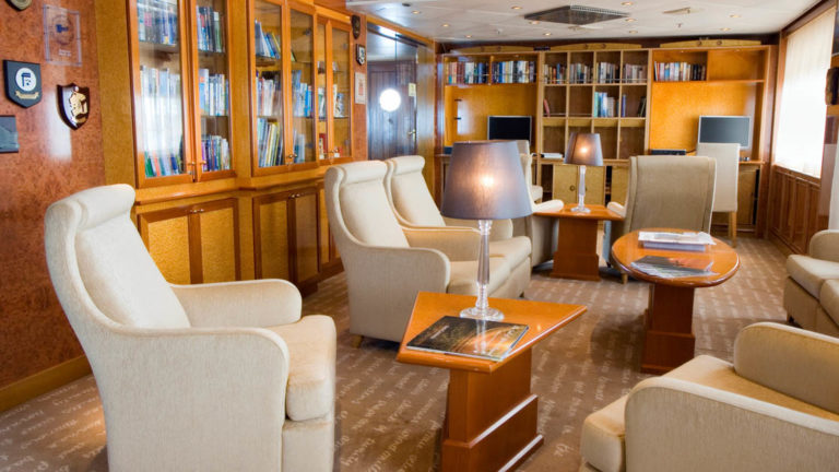 Island Sky library with large chairs, small tables, viewing windows and book shelf with assorted books.