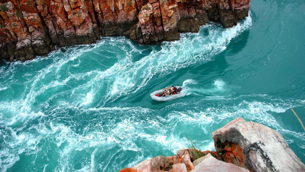 a zodiac skiff takes adventure travelers through a turquoise horizontal waterfall with cliffs on either side on the Kimberley Cruising to the Australian Outback trip