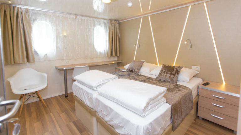 Maritimo main deck cabin with double bed, desk, 2 windows, seating, nightstand and reading light.