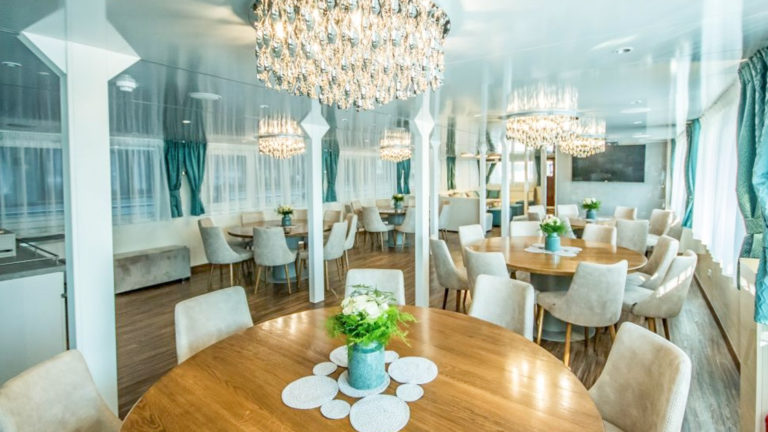 Markan Dining Room with round tables, chairs, large windows and chandeliers.