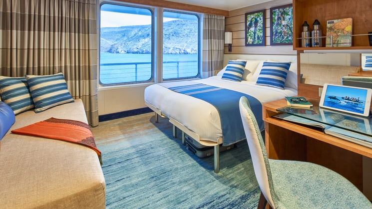 Queen bed, sofa, desk, chair and large windows in cabin aboard National Geographic Venture expedition ship