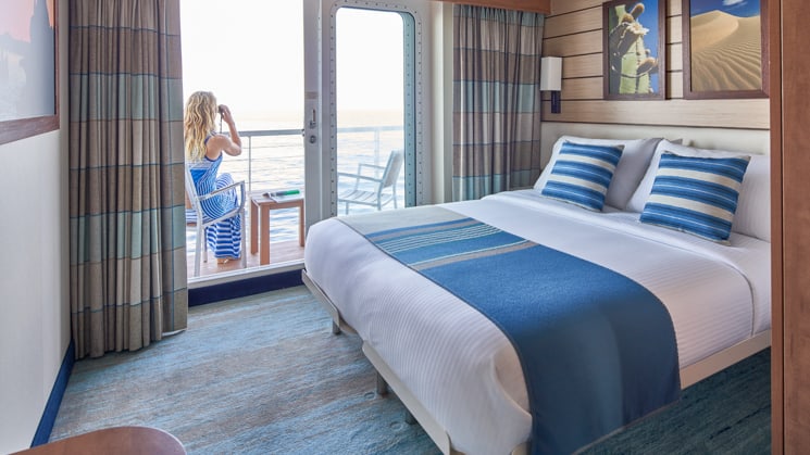 Woman sitting on private balcony of cabin with large bed aboard National Geographic Venture expedition ship
