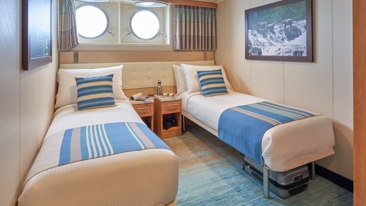 Cabin interior with two beds, nightstands, and two portholes aboard National Geographic Venture expedition ship
