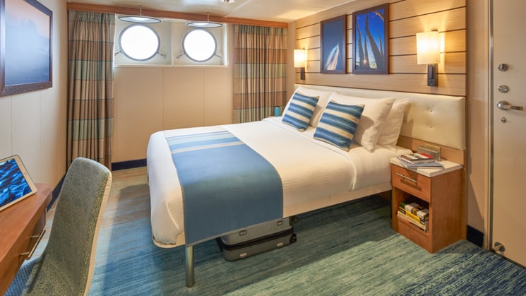 Large bed, nightstand, desk, chair and two portholes aboard National Geographic Venture expedition ship