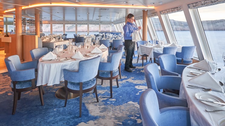Crew member sets table in window-lined dining room aboard National Geographic Venture expedition ship