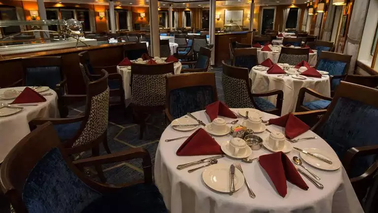 Dining room of Ocean Adventurer polar small ship, with 4-person, round tables set with fine linens & plateware.