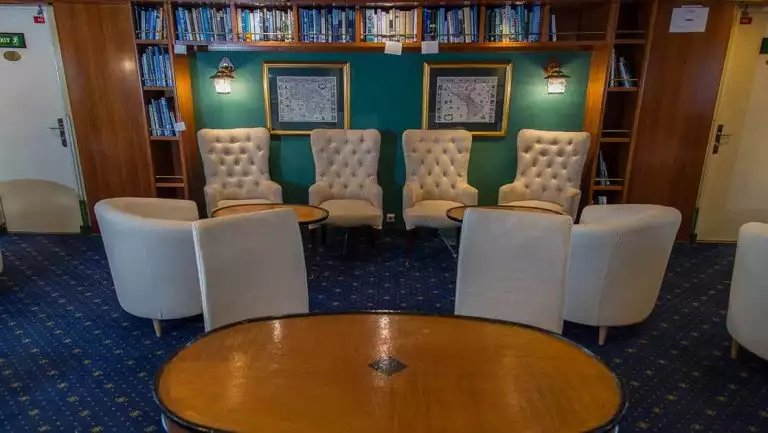 Library with beige, padded chairs, filled wooden bookshelves & wooden tables aboard Ocean Adventurer polar small ship.