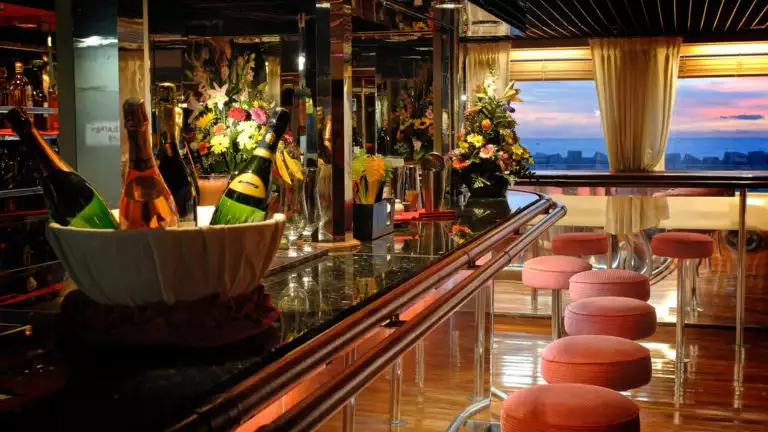 Wooden bar with red fabric barstools aboard Ocean Diamond polar ship, at sunset.