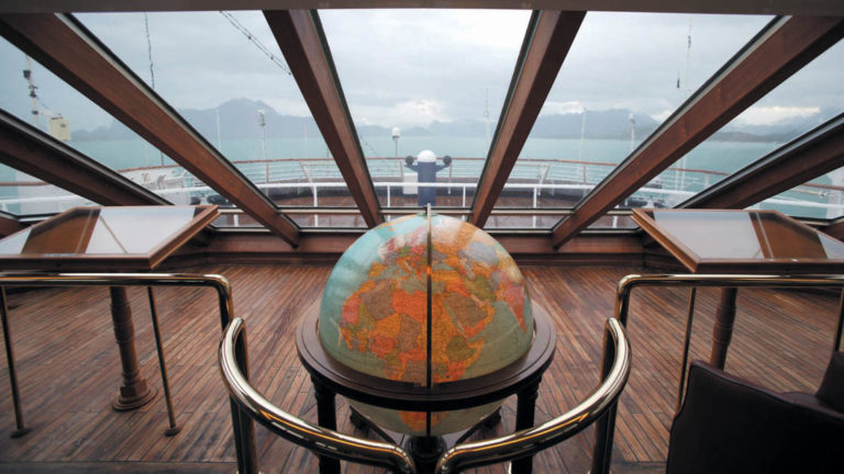 Observation lounge with large glass windows, wooden tables and a globe aboard Ocean Diamond polar small ship.