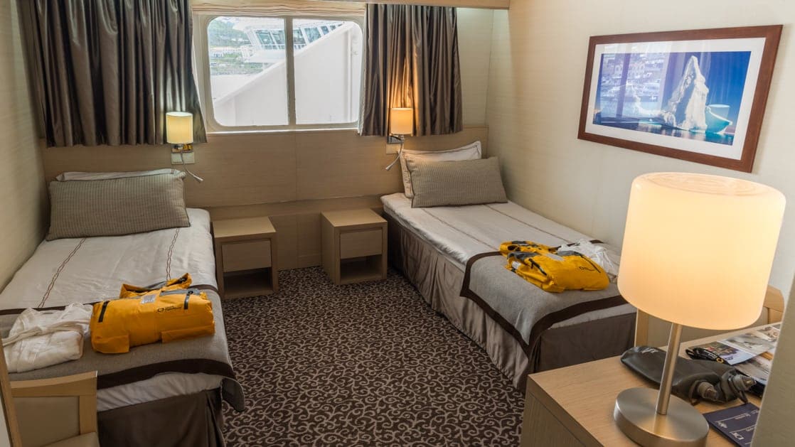 Two twin beds in a spacious room with window and side tables aboard the Ocean Diamond