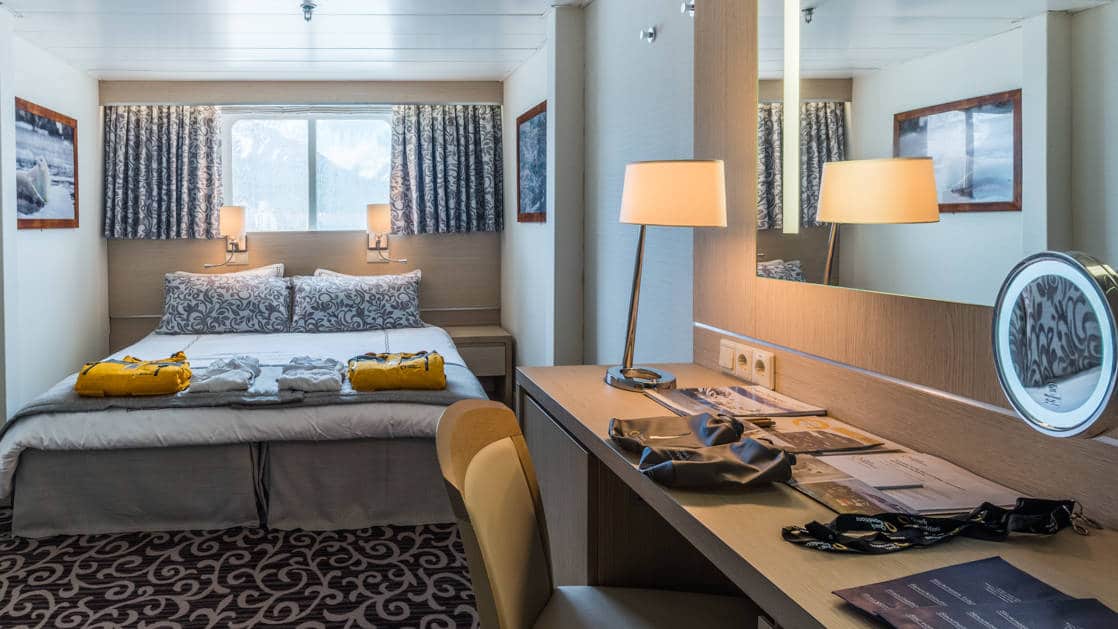 King bed with windows and folded jackets and side table aboard the Ocean Diamond