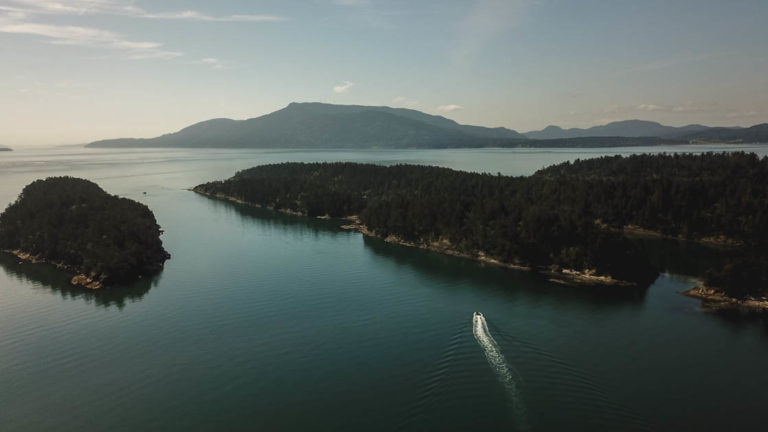 aerial view of sucia island in the pacific northwest while a small ship travels through a channel