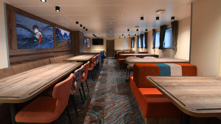 dining room with rows of tables and chairs with windows on the walls aboard the ortelius small ship