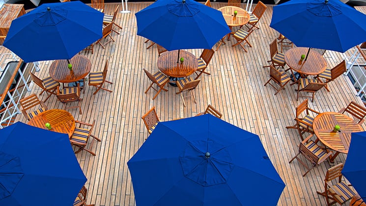 Outdoor cafe with wood furniture and blue unbrellas on the Corinthian small ship.