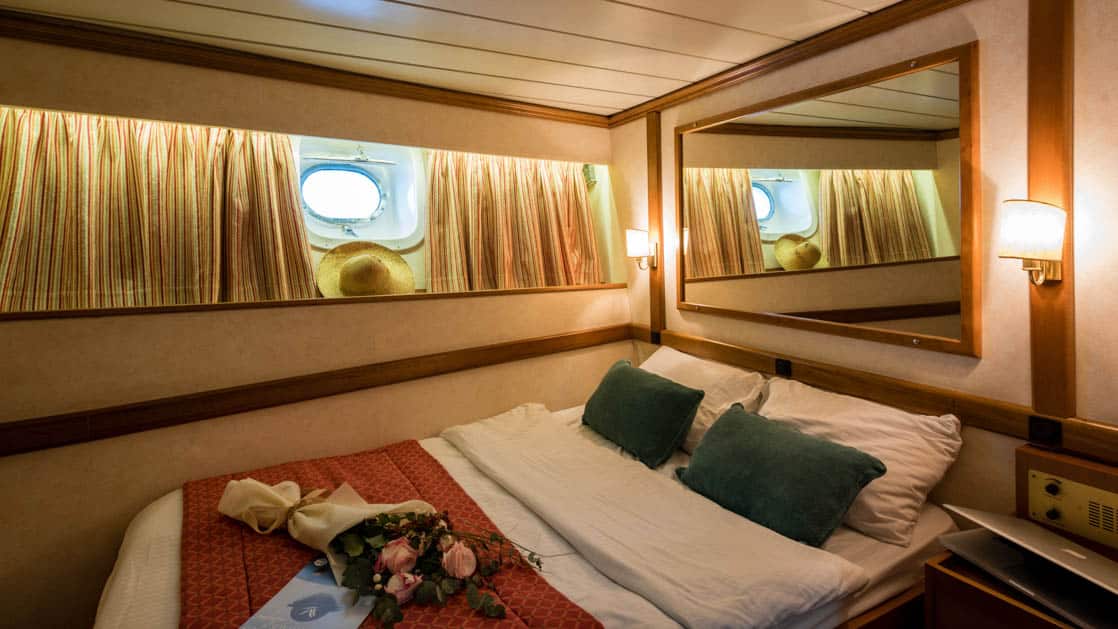 panorama Mediterranean yacht cabin with large bed, mirror above the bed and porthole window