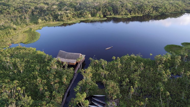 An aerial view of the Sacha Jungle Lodge, a sustainable hotel nestled in the Ecuadorian Amazon on the edge of a lake with 26 private thatched-roof cabins.