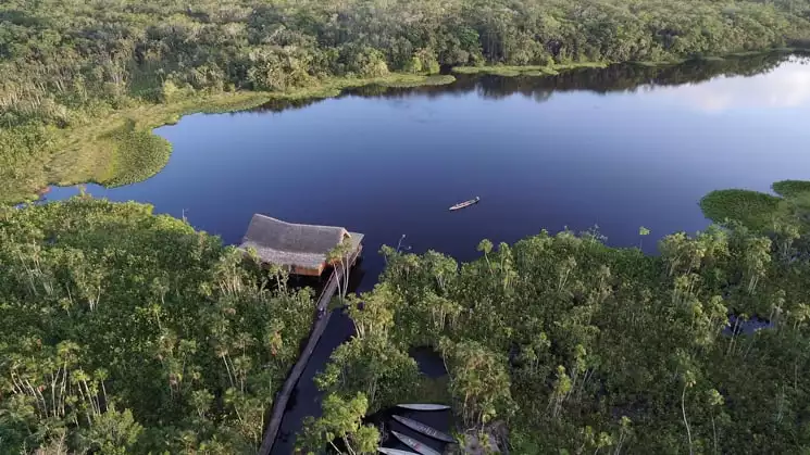 An aerial view of the Sacha Jungle Lodge, a sustainable hotel nestled in the Ecuadorian Amazon on the edge of a lake with 26 private thatched-roof cabins.