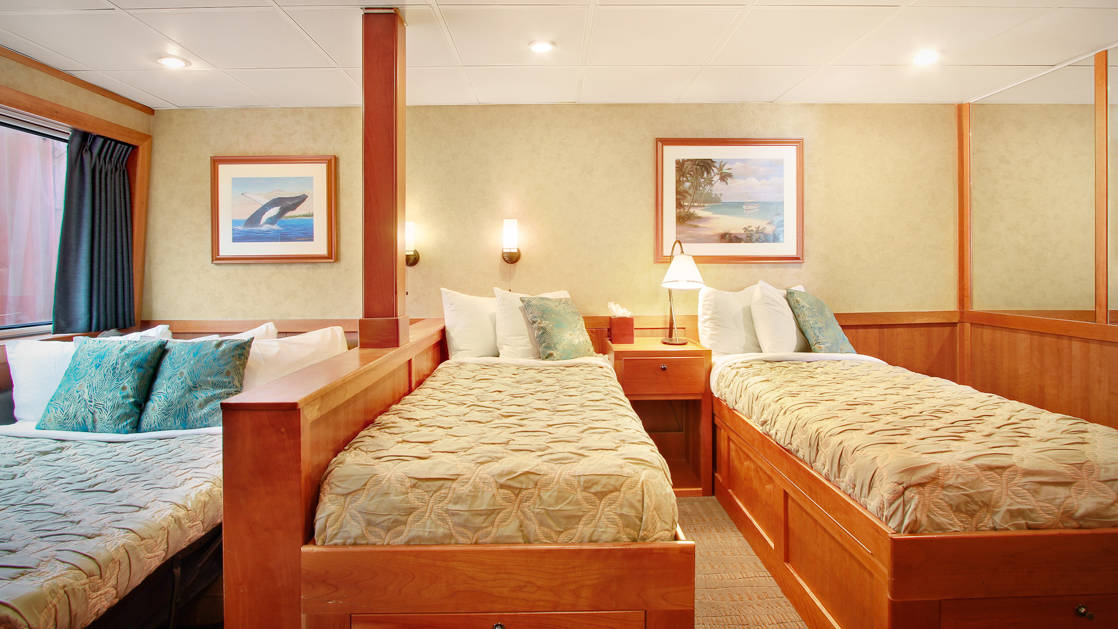 Admiral stateroom aboard the Safari Explorer Hawaii small ship, with three single beds and hanging pictures above the bed