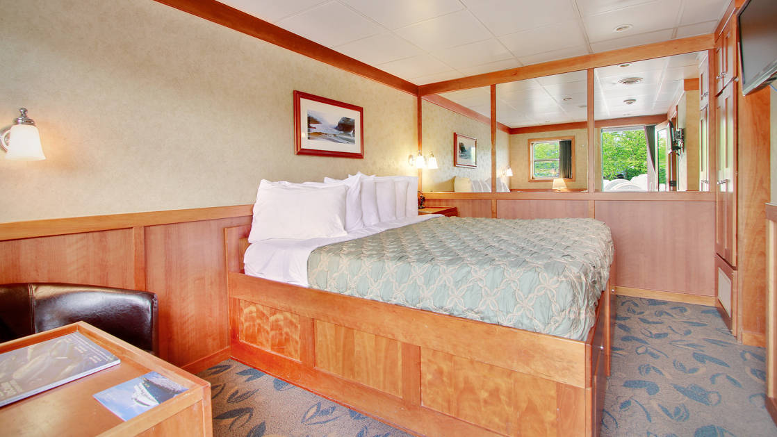 Commander stateroom cabin aboard the Safari Explorer Hawaii small ship, with a bed, comfortable chair, large mirror and pictures on the walls