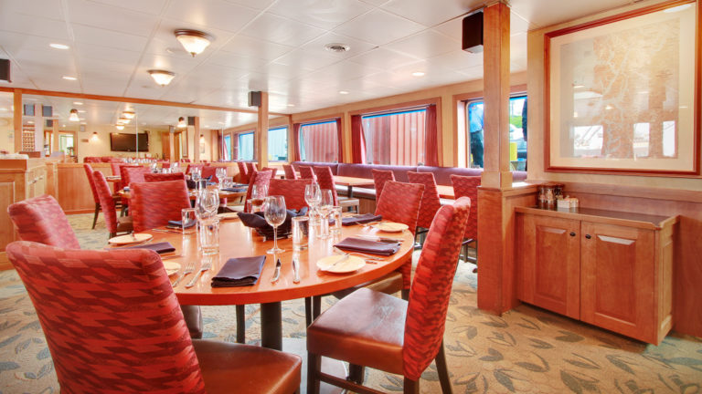 dining room with rows of tables and chairs, lined with windows aboard the Safari Explorer Hawaii small ship