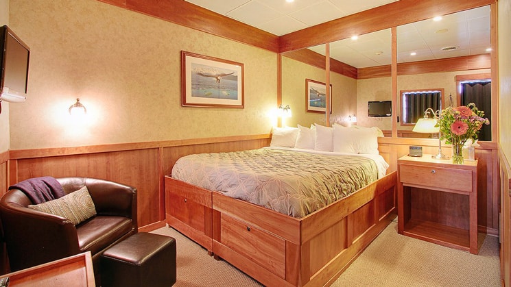 Jr Commodore stateroom with chair and foot stool with mirrors behind bed aboard the Safari Explorer Hawaii small ship