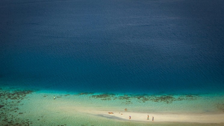 looking down at an indonesia beach at white sand, blue water and coral under the water