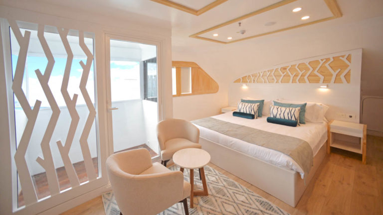 Main Deck Suite aboard Sea Star Galapagos small ship with white and cream decor, two chairs and table with balcony.