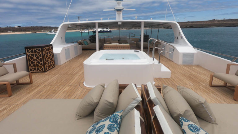 Sundeck chaise loungers with beige and blue pillows plus central hot tub aboard Sea Star Journey Galapagos small yacht.