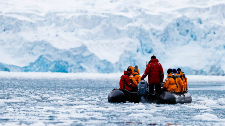 adventure travelers on the spitsbergen in depth small ship cruise trip in a zodiac skiff on icy water with an iceberg in the distance