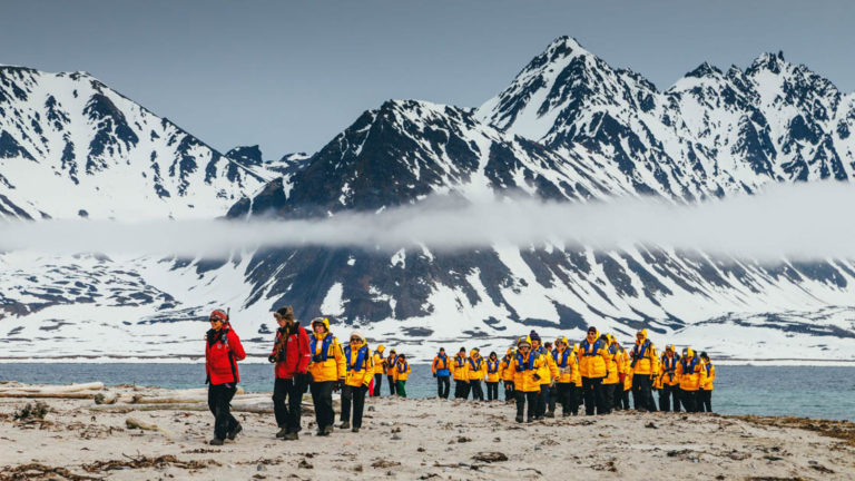 group of travelers with yellow jackets led by two guides in red on a shore excursion of the spitsbergen explorer arctic small ship cruise trip