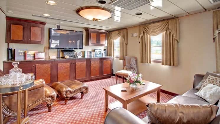 Suite living room with couch, chairs, table, TV, windows aboard Wilderness Legacy expedition ship