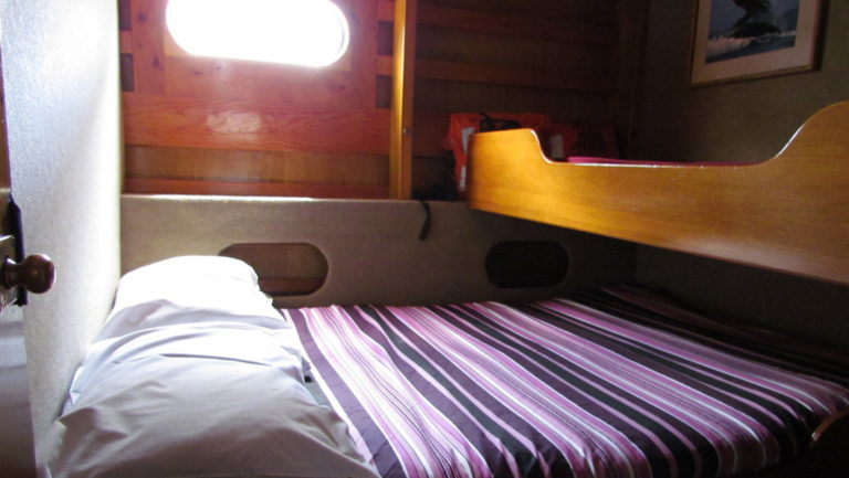 Cabin aboard Affinity with double bed and twin bed above it with small window.