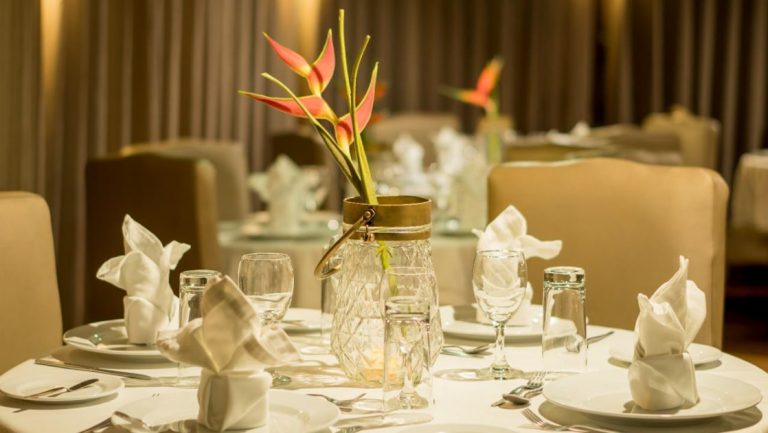 Dining room aboard Amazon riverboat Amatista, with small tables set with white tablecloths, padded beige chairs & floral centerpieces.