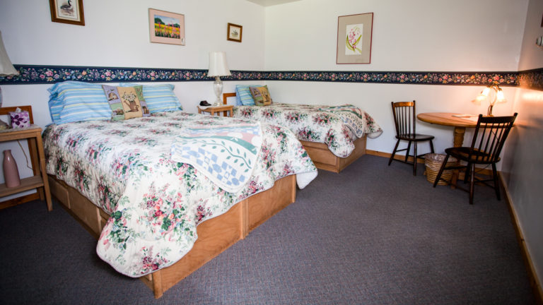 Annie Mae Lodge room with two queen beds with white quilts and a table and chairs.